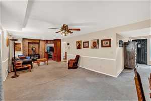 Living room featuring ceiling fan, a wood stove, brick wall, and light carpet