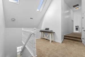 Corridor with high vaulted ceiling, light colored carpet, and a skylight