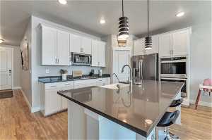 Kitchen featuring appliances with stainless steel finishes, pendant lighting, an island with sink, light hardwood / wood-style floors, and white cabinetry