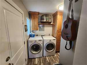 Clothes washing area featuring washing machine and dryer, cabinets, hookup for an electric dryer, and wood-type flooring