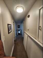 Hallway featuring dark colored carpet and a textured ceiling