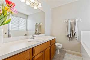 Bathroom featuring toilet, a notable chandelier, tile flooring, vanity, and a bathing tub
