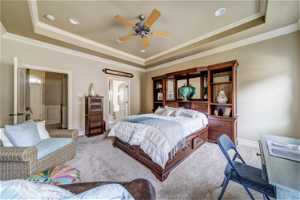 Carpeted bedroom with ensuite bath, a tray ceiling, ornamental molding, and ceiling fan