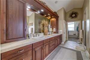 Bathroom with dual sinks, tile flooring, large vanity, and vaulted ceiling