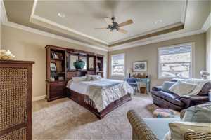 Carpeted bedroom featuring a raised ceiling, ornamental molding, and ceiling fan