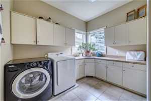 Laundry area with washing machine and clothes dryer, cabinets, and light tile flooring