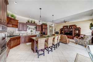 Kitchen featuring decorative light fixtures, backsplash, ceiling fan, a breakfast bar, and light stone counters
