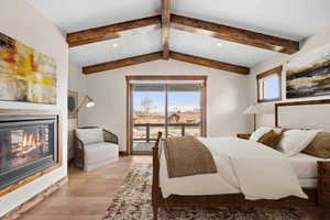 Bedroom featuring vaulted ceiling with beams, light wood-type flooring, access to outside, and multiple windows