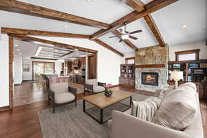 Living room featuring vaulted ceiling with beams, a fireplace, dark wood-type flooring, and ceiling fan