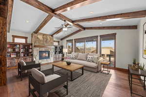 Living room with lofted ceiling with beams, ceiling fan, a stone fireplace, and dark wood-type flooring