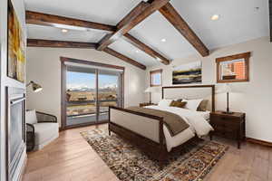 Bedroom featuring access to exterior, lofted ceiling with beams, and light hardwood / wood-style floors