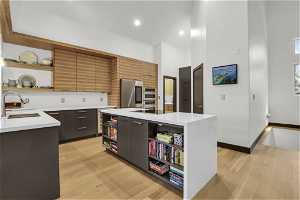Kitchen with appliances with stainless steel finishes, sink, light hardwood / wood-style flooring, dark brown cabinetry, and a center island with sink