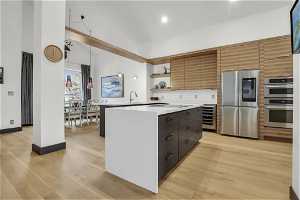 Kitchen with appliances with stainless steel finishes, light hardwood / wood-style floors, wine cooler, a center island, and pendant lighting