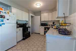 Kitchen with tasteful backsplash, white cabinets, black appliances, and light tile flooring