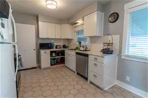 Kitchen with white refrigerator, tasteful backsplash, dishwasher, and white cabinetry