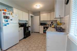 Kitchen with tasteful backsplash, white cabinets, black appliances, and light tile floors
