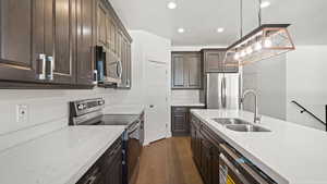 Kitchen with light stone countertops, dark wood-type flooring, stainless steel appliances, decorative light fixtures, and sink