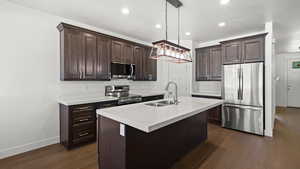 Kitchen featuring dark hardwood / wood-style floors, an island with sink, stainless steel appliances, decorative light fixtures, and sink