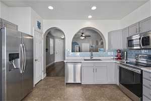 Kitchen featuring dark tile floors, tasteful backsplash, appliances with stainless steel finishes, and sink