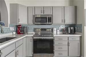 Kitchen with sink, appliances with stainless steel finishes, backsplash, and gray cabinetry