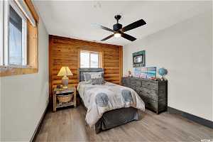 Bedroom featuring ceiling fan, light wood-type flooring, and rustic walls