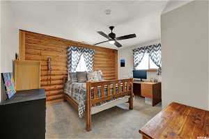 Bedroom featuring ceiling fan, light carpet, and rustic walls
