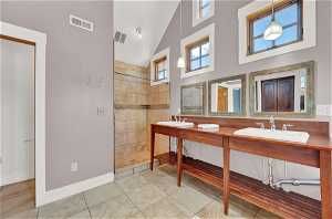 Bathroom featuring tile flooring, high vaulted ceiling, dual vanity, and tiled shower