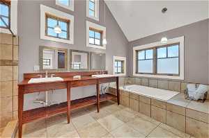 Bathroom with high vaulted ceiling, oversized vanity, tile flooring, dual sinks, and tiled bath