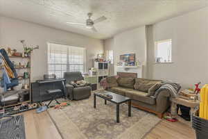 Unit 1006 - Living room with a healthy amount of sunlight, light hardwood / wood-style floors, ceiling fan, and a textured ceiling