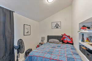 Unit 1002 - View of the second bedroom featuring a vaulted ceiling and built-in shelves.