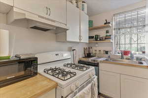 Unit 1002 - Kitchen with white range with gas stovetop, white cabinets, premium range hood, and sink