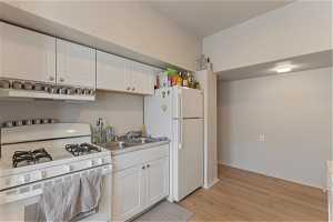Unit 1006 - Kitchen with extractor fan, white appliances, white cabinets, light wood-type flooring, and sink