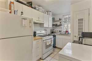 Unit 1002 - Kitchen with white appliances, white cabinets, sink, and light tile flooring