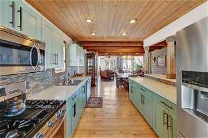 Kitchen with appliances with stainless steel finishes, light hardwood / wood-style flooring, hanging light fixtures, wooden ceiling, and sink