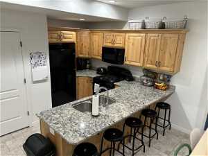 Kitchen with light stone countertops, black appliances, kitchen peninsula, a kitchen bar, and light tile floors