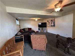 Carpeted living room featuring ceiling fan and a textured ceiling