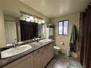 Bathroom featuring tile floors, toilet, dual bowl vanity, and a textured ceiling