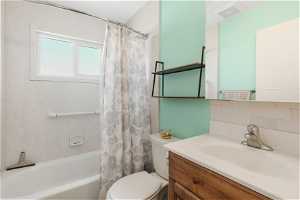 Full bathroom with tile walls, shower / tub combo, backsplash, toilet, and vanity with extensive cabinet space