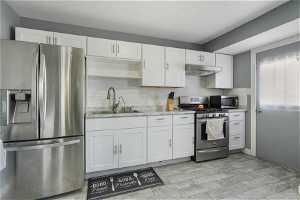 Kitchen with white cabinets, sink, appliances with stainless steel finishes, and backsplash