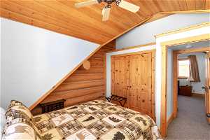 Carpeted bedroom featuring a closet, log walls, vaulted ceiling, wood ceiling, and ceiling fan