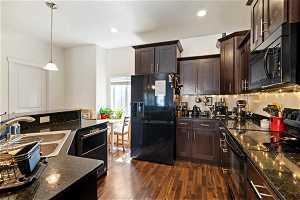 Kitchen with hanging light fixtures, dark wood-type flooring, sink, dark brown cabinets, and black appliances