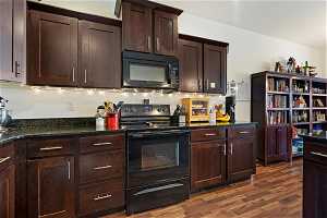 Kitchen with dark stone counters, dark brown cabinetry, black appliances, and dark wood-style flooring