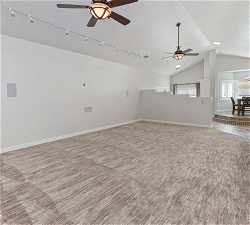 Unfurnished living room featuring rail lighting, light colored carpet, ceiling fan, and lofted ceiling