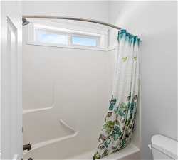 Bathroom with plenty of natural light, shower / bath combination with curtain, and toilet