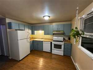 Kitchen featuring a baseboard heating unit, white appliances, wood-type flooring, sink, and blue cabinets