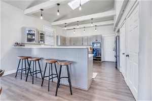 Kitchen with gray cabinets, light hardwood / wood-style flooring, lofted ceiling with skylight, kitchen peninsula, and stainless steel appliances