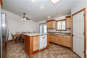 Kitchen with ceiling fan, light tile floors, dishwasher, stainless steel fridge with ice dispenser, and vaulted ceiling