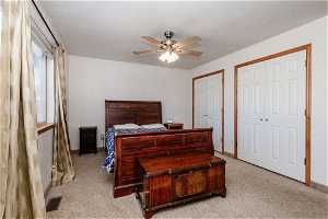 Owner's suite Bedroom featuring two closets, ceiling fan, and light carpet and wood stained trim.