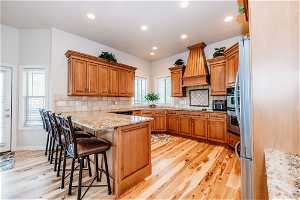 Kitchen featuring light hardwood / wood-style flooring, backsplash, premium range hood, and a breakfast bar