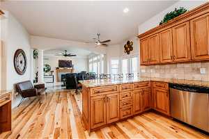 Kitchen with ceiling fan, light hardwood / wood-style floors, tasteful backsplash, stainless steel dishwasher, and light stone countertops